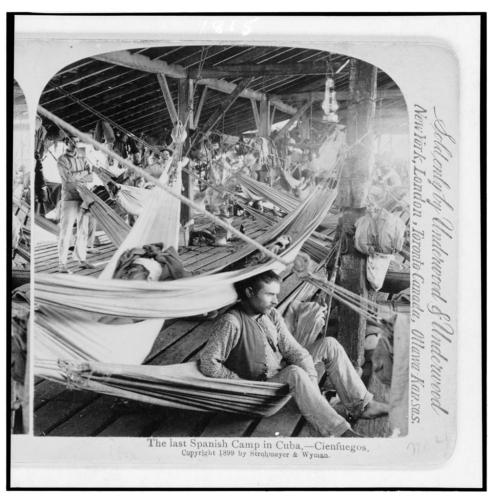 El último campamento español en Cuba - CienfuegosResumenHombres en hamacas dentro de un refugio de madera.1899